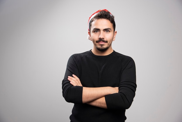 Jonge man in de rode hoed van de Kerstman die zich over een grijze muur bevindt.