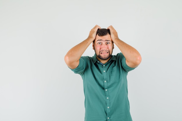 Jonge man in een groen shirt die de hand op zijn hoofd houdt en er verontrust uitziet, vooraanzicht.