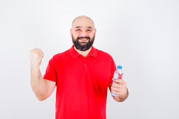 Jonge man in een rood shirt met fles terwijl hij een succesgebaar toont en er gelukkig uitziet, vooraanzicht.