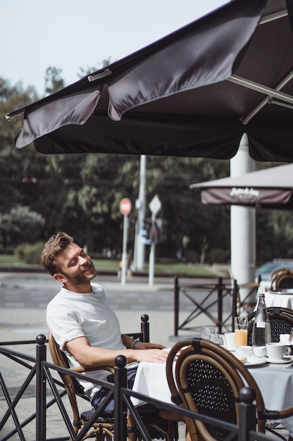 Gratis foto jonge man in een zomercafé op het terras ontbijt