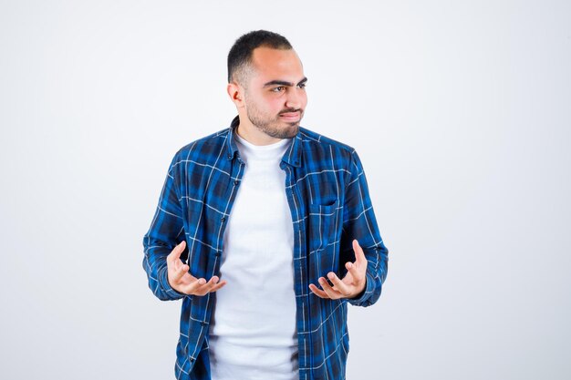 Jonge man in geruit overhemd en wit t-shirt die zijn handen uitrekt terwijl hij iets ontvangt en er geïrriteerd uitziet