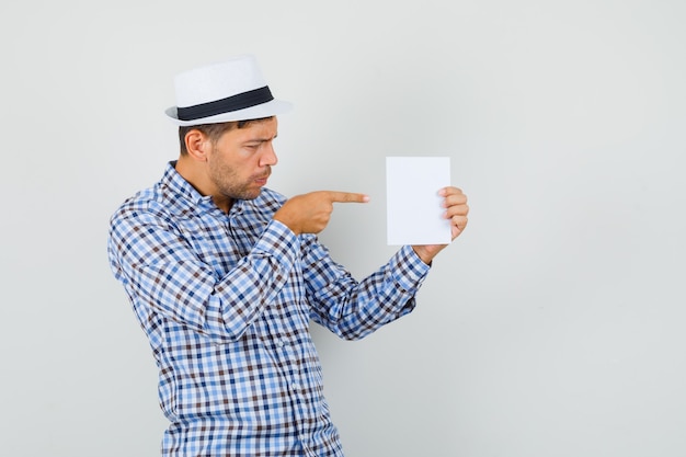 Jonge man in geruit overhemd, hoed wijzend op vel papier en kijkt gefocust