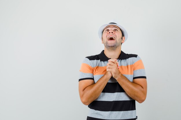 Jonge man in gestreept t-shirt, hoed met biddend gebaar en op zoek naar hoopvolle ruimte voor tekst
