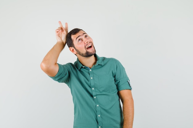 Jonge man in groen shirt die v-teken op zijn hoofd maakt en er grappig uitziet, vooraanzicht.