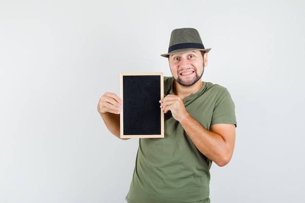 Jonge man in groen t-shirt en hoed met bord en schattig kijken