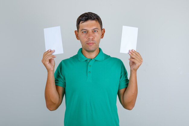 Jonge man in groen t-shirt met blanco vellen papier, vooraanzicht.