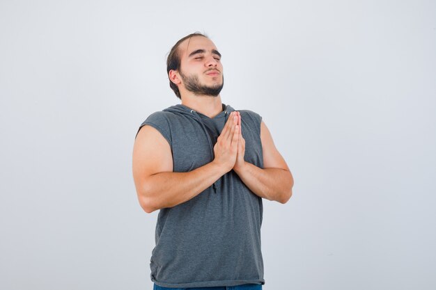 Jonge man in hoodie namaste gebaar tonen en kijkt tevreden, vooraanzicht.