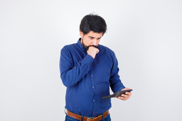 Jonge man in koningsblauw shirt berekent terwijl hij denkt, vooraanzicht.