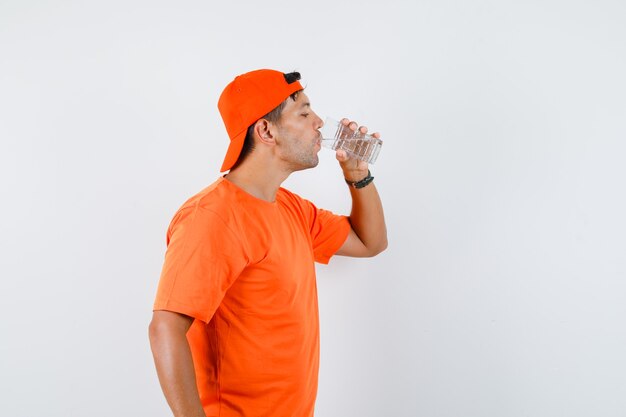 Jonge man in oranje t-shirt en pet drinkwater