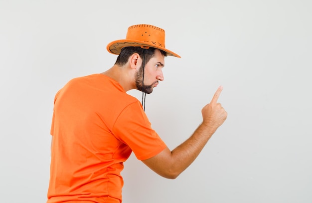 Jonge man in oranje t-shirt, hoed die iemand met vinger waarschuwt en woedend kijkt.