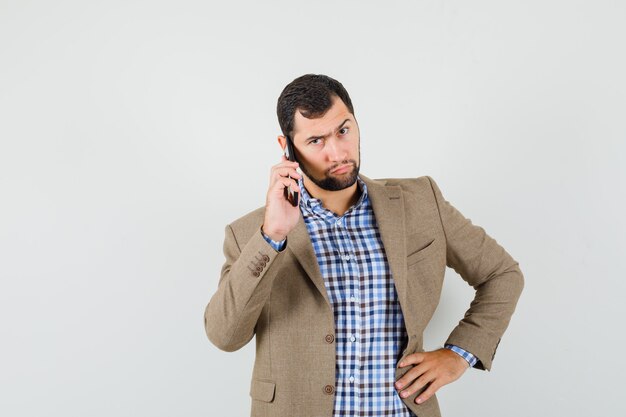 Jonge man in overhemd, jasje praten op mobiele telefoon en op zoek ernstig, vooraanzicht.