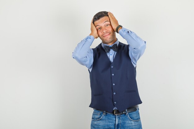 Jonge man in pak, spijkerbroek hoofd met handen te houden en optimistisch op zoek