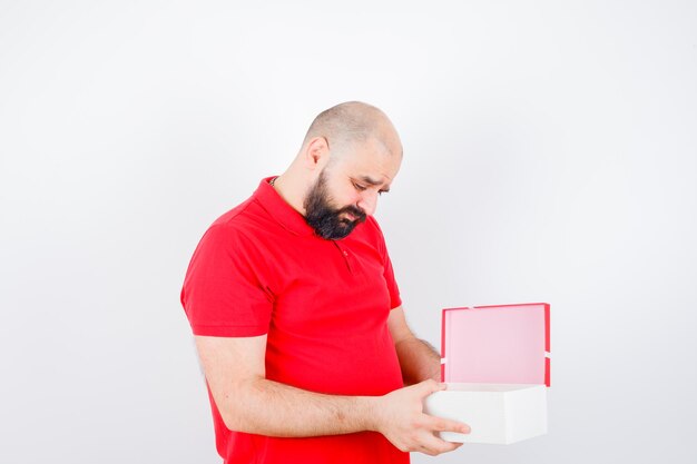 Jonge man in rood shirt die in de doos kijkt en er verstandig uitziet.