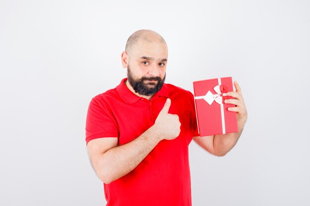 Jonge man in rood shirt met huidige doos terwijl duim omhoog, vooraanzicht.