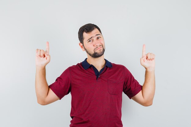 Jonge man in rood t-shirt die omhoog wijst en ontevreden, vooraanzicht kijkt.