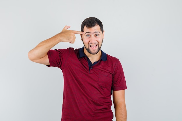 Jonge man in rood t-shirt wijzend op zijn hoofd en op zoek raar, vooraanzicht.