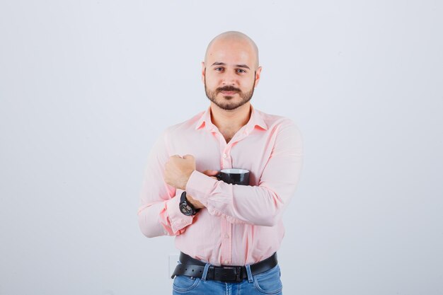 Jonge man in roze shirt, jeans knuffelen zijn kopje, vooraanzicht.