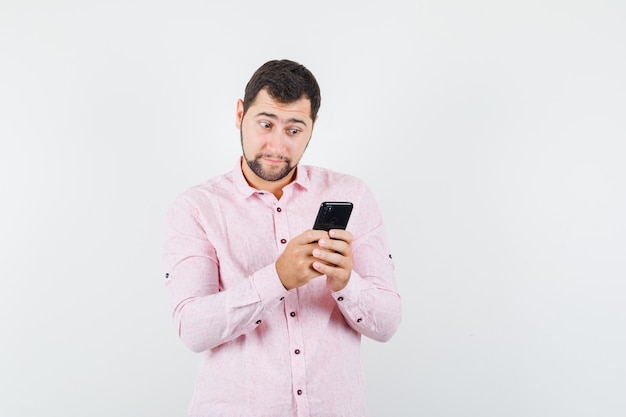 Jonge man in roze shirt met behulp van mobiele telefoon en vraagt zich af