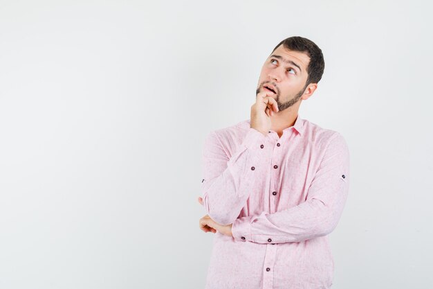 Jonge man in roze shirt opzoeken en nadenkend kijken