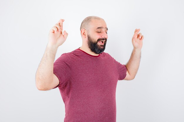 Jonge man in roze t-shirt die gekruiste vingers opsteekt terwijl hij glimlacht.