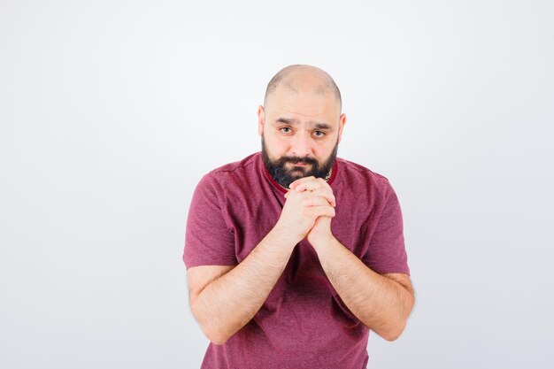 Jonge man in roze t-shirt die handen in gebedspositie omklemt en er gefocust uitziet, vooraanzicht.