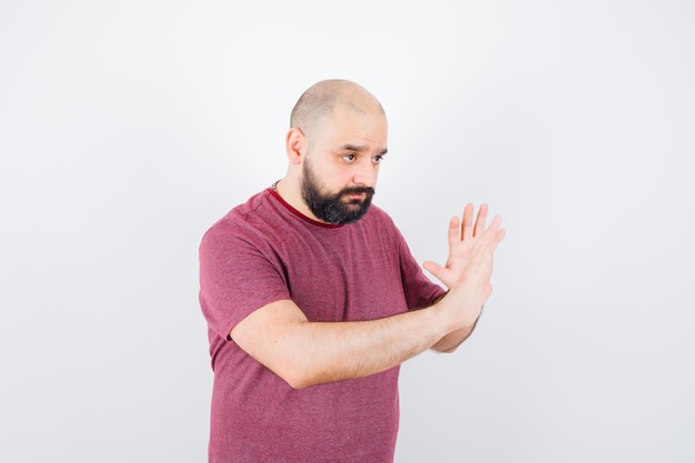 Jonge man in roze t-shirt die handen opsteekt om te verdedigen en er voorzichtig uit te zien, vooraanzicht.