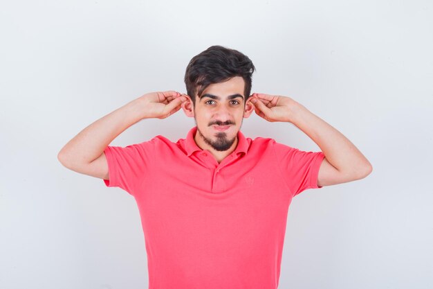 Jonge man in roze t-shirt die oren naar beneden trekt en er schattig uitziet, vooraanzicht.