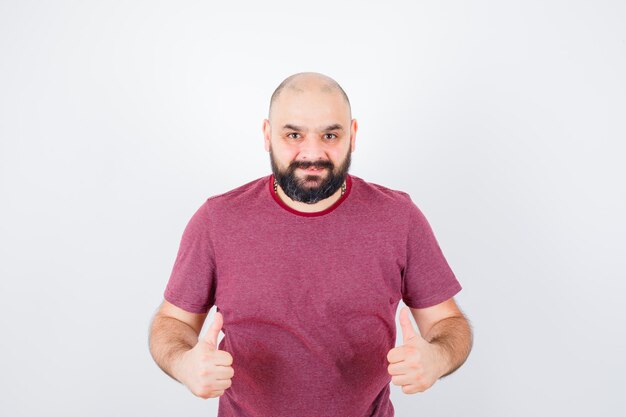 Jonge man in roze t-shirt met duim omhoog en blij, vooraanzicht.