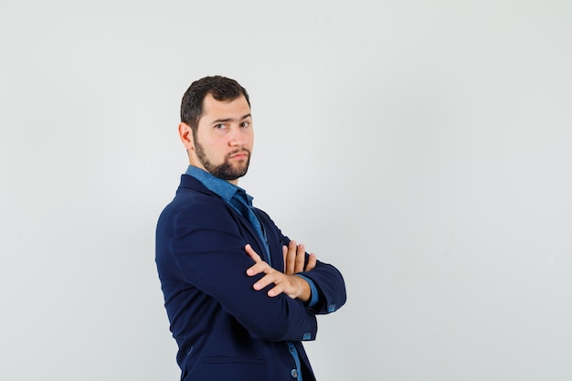 Jonge man in shirt, jasje permanent met gekruiste armen en op zoek naar strikte.