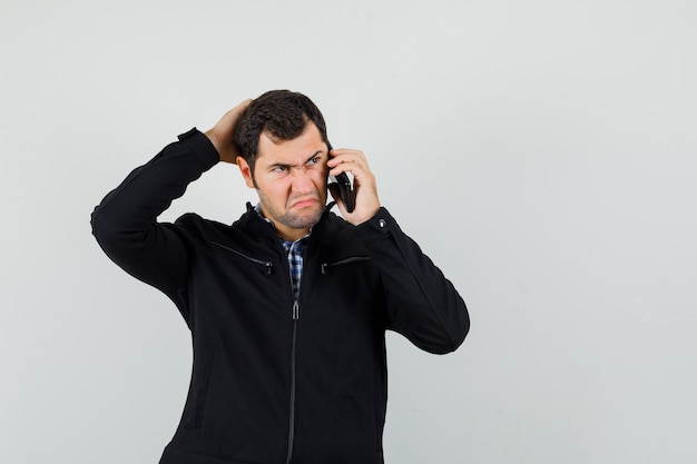 Jonge man in shirt, jasje praten op mobiele telefoon en op zoek attent