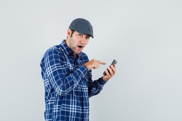 Jonge man in shirt, pet met behulp van rekenmachine en aarzelend, vooraanzicht op zoek.