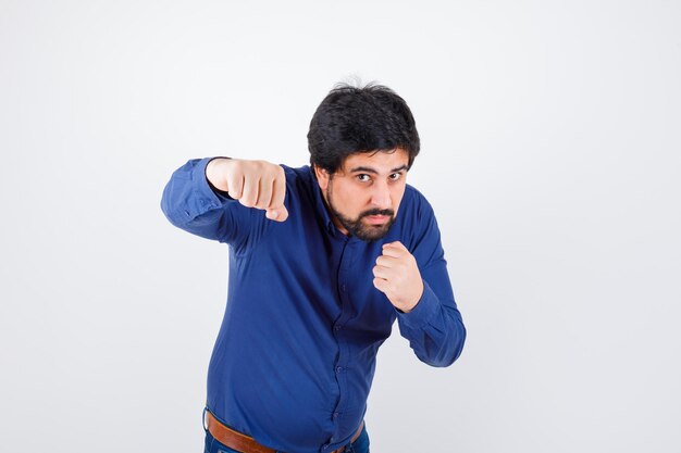 Jonge man in shirt, spijkerbroek die in vechthouding staat en er zelfverzekerd uitziet, vooraanzicht.