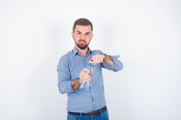 Jonge man in shirt, spijkerbroek plastic waterfles openen en op zoek zelfverzekerd, vooraanzicht.