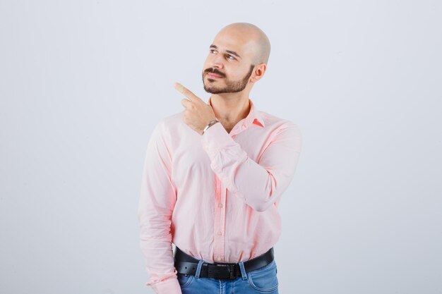 Jonge man in shirt, spijkerbroek wijzend naar de linkerbovenhoek en zelfverzekerd, vooraanzicht.