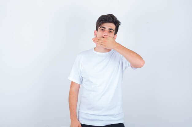 Jonge man in t-shirt die de mond bedekt met de hand en er zelfverzekerd uitziet