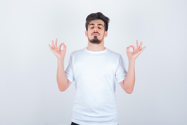 Jonge man in t-shirt die meditatiegebaar toont en er vredig uitziet