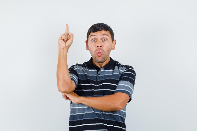 Jonge man in t-shirt die omhoog wijst en er bang uitziet, vooraanzicht.