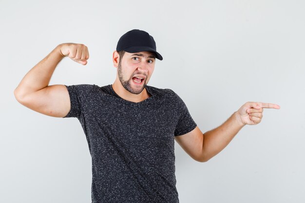 Jonge man in t-shirt en pet die vuist opheft terwijl hij naar de zijkant wijst en er zelfverzekerd uitziet