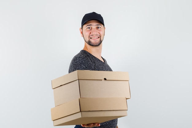 Gratis foto jonge man in t-shirt en pet met kartonnen dozen en op zoek vrolijk