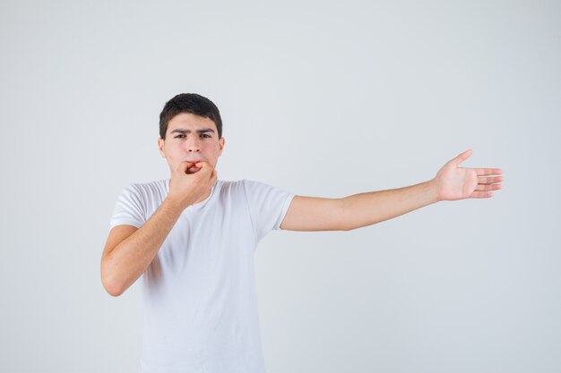 Jonge man in t-shirt fluiten op duim en wijsvinger en kijkt zelfverzekerd, vooraanzicht.