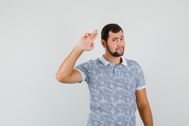 Jonge man in t-shirt gebaren met twee vingers en op zoek zelfverzekerd, vooraanzicht.