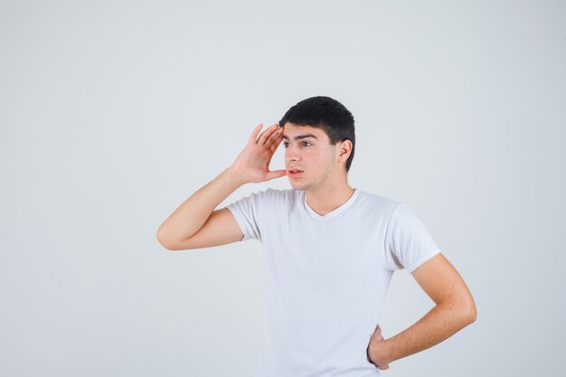 Jonge man in t-shirt hand boven het hoofd en op zoek gericht, vooraanzicht.