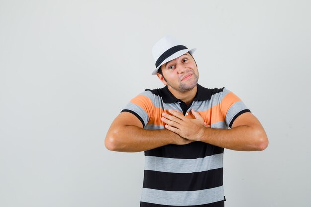 Jonge man in t-shirt, hoed hand in hand op zijn borst en ongemakkelijk op zoek