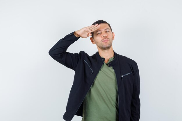 Jonge man in t-shirt, jas die een groetgebaar maakt en er zelfverzekerd uitziet, vooraanzicht.