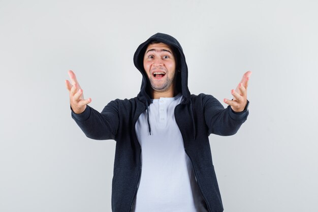 Jonge man in t-shirt, jas openen armen voor knuffel en op zoek vrolijk, vooraanzicht.