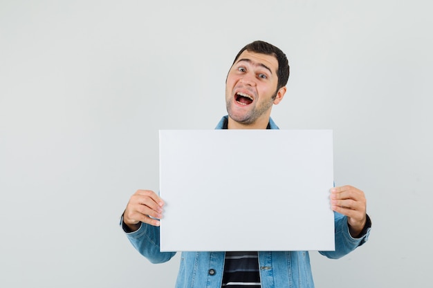 Jonge man in t-shirt, jasje met leeg canvas en op zoek blij