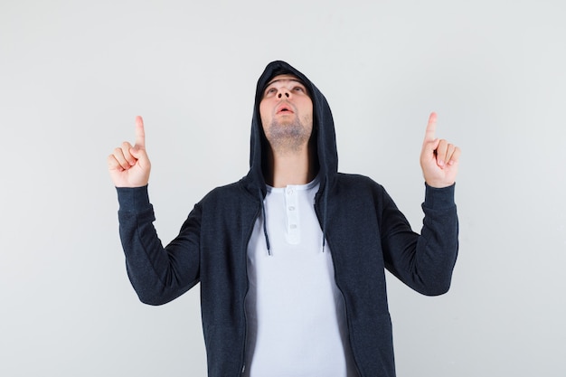 Jonge man in t-shirt, jasje naar boven en op zoek dankbaar, vooraanzicht.