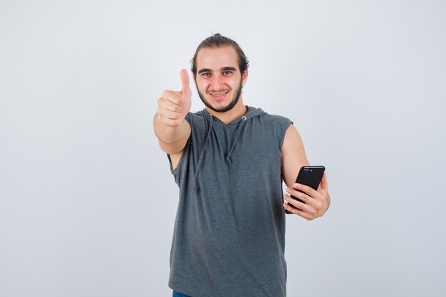Jonge man in t-shirt met een kap die duim toont en tevreden, vooraanzicht kijkt.