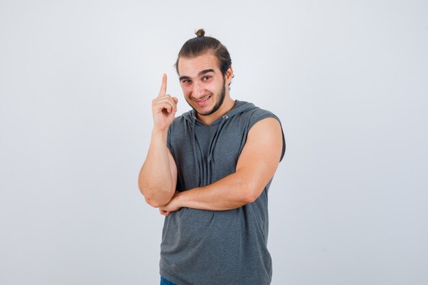 Jonge man in t-shirt met een kap die omhoog wijst en gelukkig, vooraanzicht kijkt.