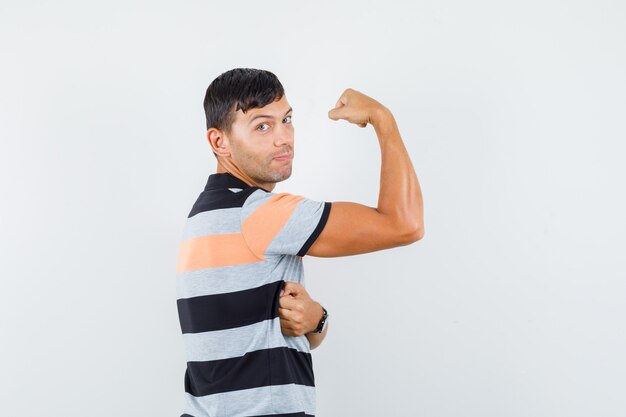 Jonge man in t-shirt met spieren van de arm en op zoek naar sterk